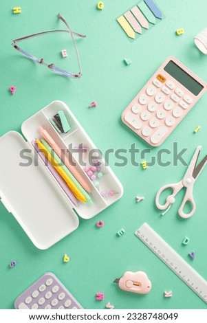 Colorful back-to-school assortment. Vertical top view of feminine stationery, pencil case, pens, sticky notes, clerical knife, scissors, calculator, ruler, glasses, alphabet letters on teal backdrop