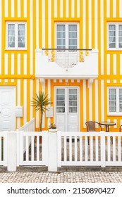 Colorful beautiful striped yellow house facade with doors, windows, terrace, mailbox, and palm tree in a fishing village near the ocean in Portugal