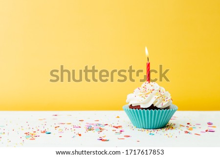 A colorful  birthday cupcake with one candle and confetti on a yellow background