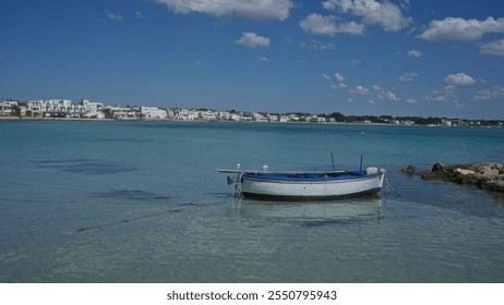 Colorful boat floating on turquoise water next to a rocky shore in porto cesareo, puglia, italy, with a backdrop of white buildings and a bright blue sky filled with fluffy clouds. - Powered by Shutterstock