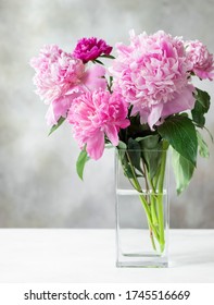 colorful bouquet of assorted peonies in a square glass vase on a white table. Cozy home concept. vertical image. place for text