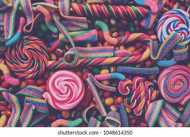 Colorful Bright Assorted  Candy Canes And Rainbow Colored Spiral Lollipops  With Scattered Marmalade, Jellybeans And Different Colored Round Candy. Top View. Candy Background.