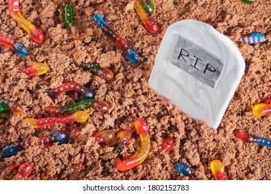 Colorful And Bright Assorted Gummy Worms In Chocolate Cake Ground Around A Sugar Tombstone, Halloween Party Food