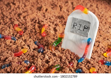 Colorful And Bright Assorted Gummy Worms In Chocolate Cake Ground Around A Sugar Gravestone, Halloween Party Fun Food