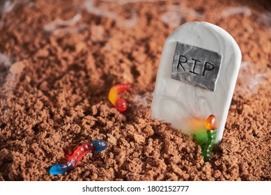 Colorful And Bright Gummy Worms In Chocolate Cake Ground Around A Sugar Gravestone, Halloween Party Fun Food