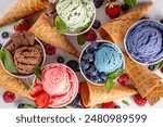 Colorful bright ice cream on bowls, with waffle cones and berries, on white background. Variety of ice cream portions with different flavor with fresh berries top view copy space layout background