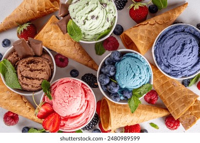 Colorful bright ice cream on bowls, with waffle cones and berries, on white background. Variety of ice cream portions with different flavor with fresh berries top view copy space layout background