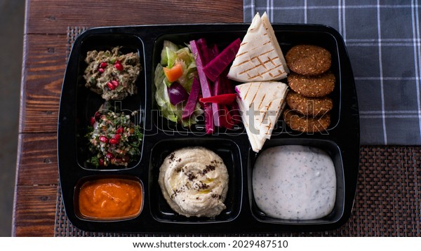 Colorful and bright Israeli dish with hummus,\
sauses, cakes and cookies in a black divided plate flat lay\
top-down composition