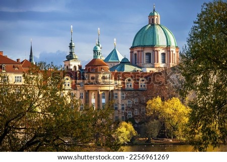 Colorful building of Prague Old town, Church of St. Francis of Assisi with green cupola, yellow autumn tree on embankment, river Vltava, Czech republic.