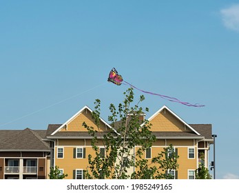 A Colorful Butterfly Kite Flies Above An Unidentified Multifamily Residence Building In An Almost-cloudless Sky