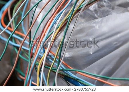 Colorful cable wire tangle creates messy chaos of electricity connections next to clear plastic bag evoking confusing and frustrating feeling of disorganization and technological junk