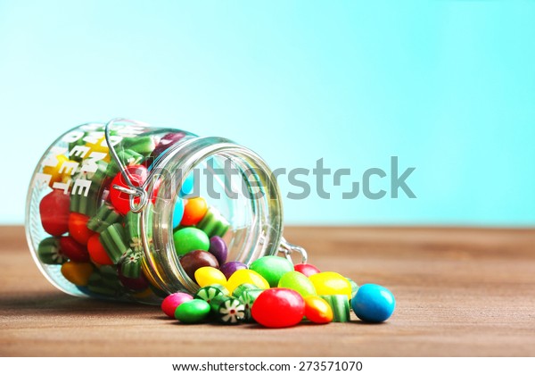 Colorful\
candies in jar on table on blue\
background