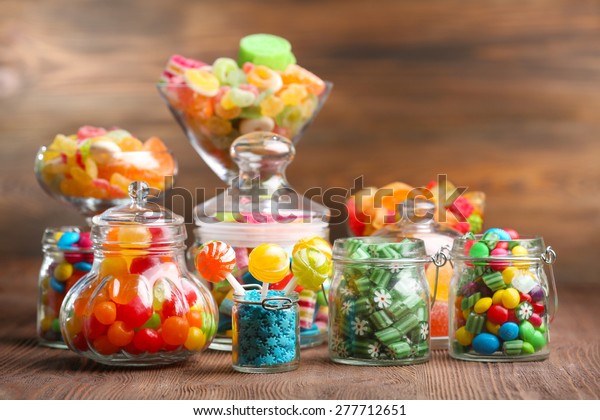 Colorful\
candies in jars on table on wooden\
background
