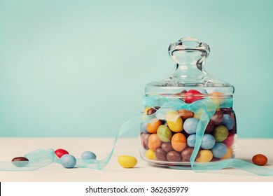 Colorful candy jar decorated with bow ribbon against blue background, gifts for Birthday or Easter