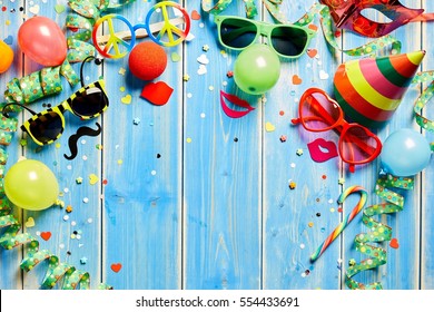 Colorful carnival frame of bright photo booth accessories, streamers, party hat and confetti on rustic blue wooden planks with central copy space