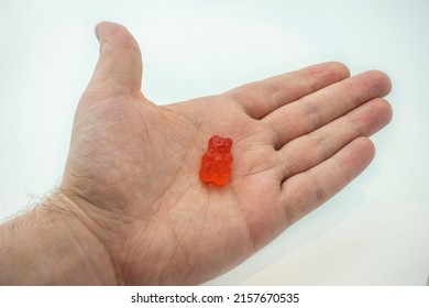A colorful CBD infused medicinal candy gummy used for healing in the palm of a male han against a plain white background