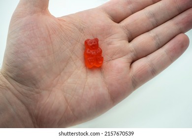 A colorful CBD infused medicinal candy gummy used for healing in the palm of a male han against a plain white background