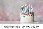 Colorful celebration birthday cake with sugar sprinkles and colorful birthday candles against a background of defocused fairy lights