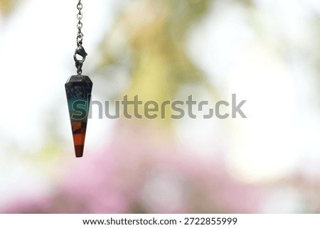 A colorful chakra pendulum, featuring layers of different stones, is shown against a luminous, ethereal bokeh background.
