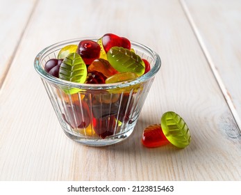 Colorful Chewy Candy In A Glass Bowl On A White Wooden Table. Multicolored Gummy Sweets Made Of Fruit Juice, Sugar And Gelatin. Confectionery And Jelly Chews Concepts. Close-up. Front View.