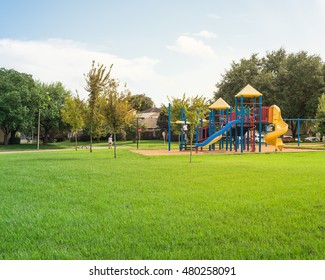 Colorful children playground activities in public park surrounded by green trees at sunset in Houston, Texas. Children run, slide, swing on modern playground. Urban neighborhood childhood concept.