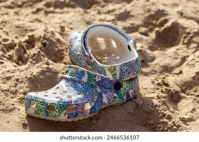 Colorful children's shoe with a pattern of leaves and geometric shapes lying abandoned on a sandy beach. The shoe appears partially buried, playful day or the transient nature of childhood moments - Powered by Shutterstock