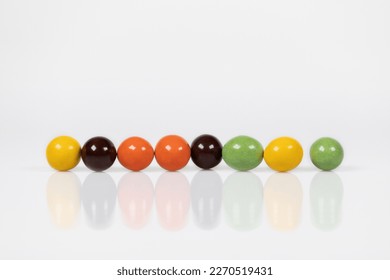 Colorful chocolate balls arranged in a row. The reflection of chocolate balls on the surface