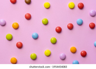 Colorful chocolate candies smarties background.Top view sweets multicolored food texture, on pink background.