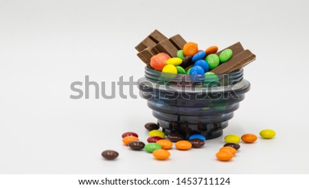 colorful chocolate granules in a glass, placed on a whaite background.