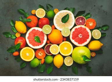 Colorful citrus fruis, food background, top view. Mix of different whole and sliced fruits: orange, grapefruit, lemon, lime and other with leaves on  green stone table