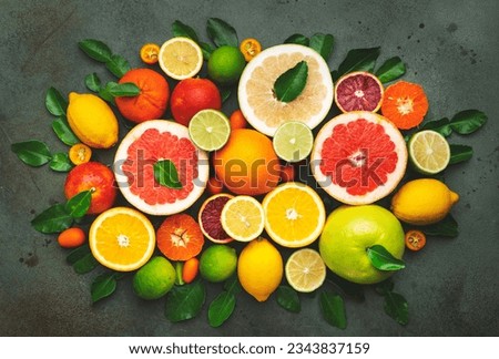 Colorful citrus fruis, food background, top view. Mix of different whole and sliced fruits: orange, grapefruit, lemon, lime and other with leaves on  green stone table