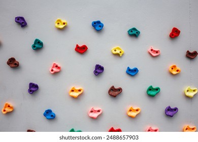 Colorful climbing holds arranged in a neat pattern on a light gray wall, perfect for indoor climbing enthusiasts and gym, Mountaineers prioritize secure activity through expert training and safety - Powered by Shutterstock