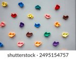 Colorful climbing wall holds arranged on grey background, showcasing variety in shapes and colors for indoor bouldering and rock climbing activities.