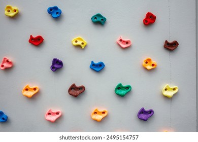 Colorful climbing wall holds arranged on grey background, showcasing variety in shapes and colors for indoor bouldering and rock climbing activities. - Powered by Shutterstock