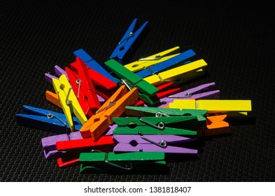 Colorful clothe pins clutter together on black background.