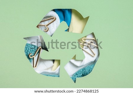Colorful clothes and mini hungers under paper cut recycling symbol. Second hand, clothing donation and recycling concept.