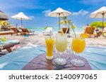 Colorful cocktails on luxury beach resort. Blurred poolside, chairs, beds under umbrella and palm tree leaves. Tropical island beachfront, infinity pool, summer vibes, cool drink glasses