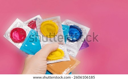 Colorful condoms in hand on pink background. High quality photo