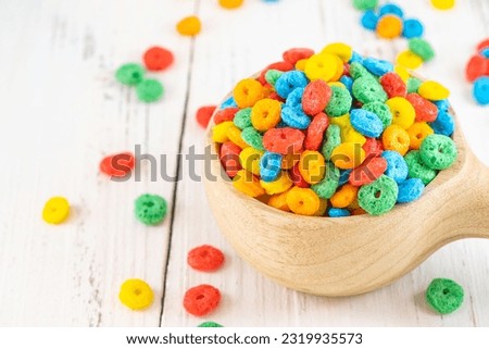 Colorful corn rings in bowl on white wooden table. Top view of bowl with fruit cereal naturally and artificially fruit flavored sweetened corn puffs. Cereal fruity shapes
