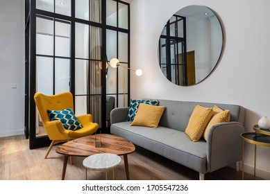 Colorful and cozy living room with a designer armchair and sofa along with a round decorative mirror and glass wall. - Shutterstock ID 1705547236