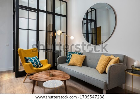 Colorful and cozy living room with a designer armchair and sofa along with a round decorative mirror and glass wall.