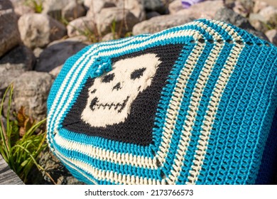 A colorful craft crocheted pillow, multicolored; black, blue, and white color cotton wool. The textile pattern in the handmade pillow is a skull with six sides and tidy stitches. 