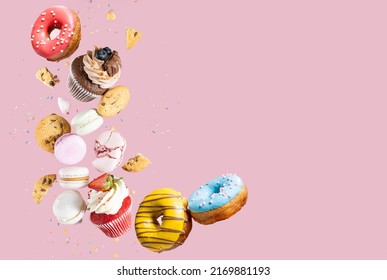 Colorful decorated Broken chocolate chip cookies, cupcakes and macaroons falling in motion on pink background with sprinkling and pieces with crumbs. Sweet and various pastries flying. - Shutterstock ID 2169881193