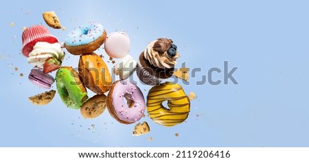 Colorful decorated donuts, cupcakes and macaroons falling in motion on blue background with sprinkling. Sweet and various doughnuts flying on pastel backdrop. Banner