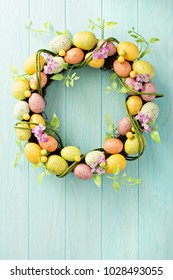 Colorful decorative Easter eggs wreath on light blue wooden background