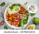 A colorful and delicious vegetarian bowl packed with fresh ingredients: avocado slices, chickpeas, leafy green spinach, cubes tomatoes and potatos create a delightful, healthy and nutritious meal.