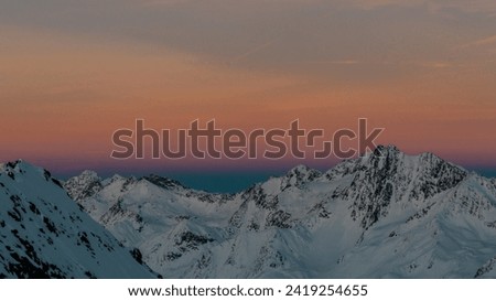 Colorful display behind the wintry mountains: A spectacular interplay of warm and cool hues bathes the mountain landscape in picturesque light.