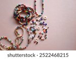 Colorful DIY necklaces, friendship bracelets and various plastic beads on pastel pink background. Flat lay.