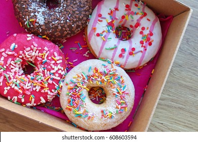 Colorful Donuts In Box On Wooden Table. Top View With Free Copy Space.