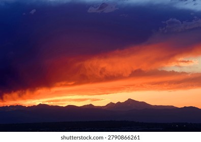 colorful, dramatic sunset and dark clouds over long's peak and the front range of the colorado rocky mountains, as seen from broomfield, colorado